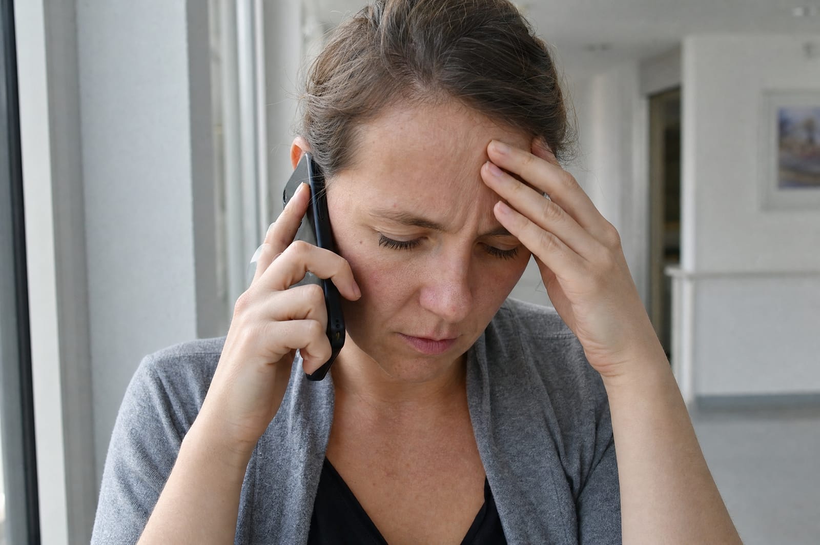 Erwachsene Tochter telefoniert auf dem Krankenhausflur, die Hand an der Stirn, den Blick gesenkt
