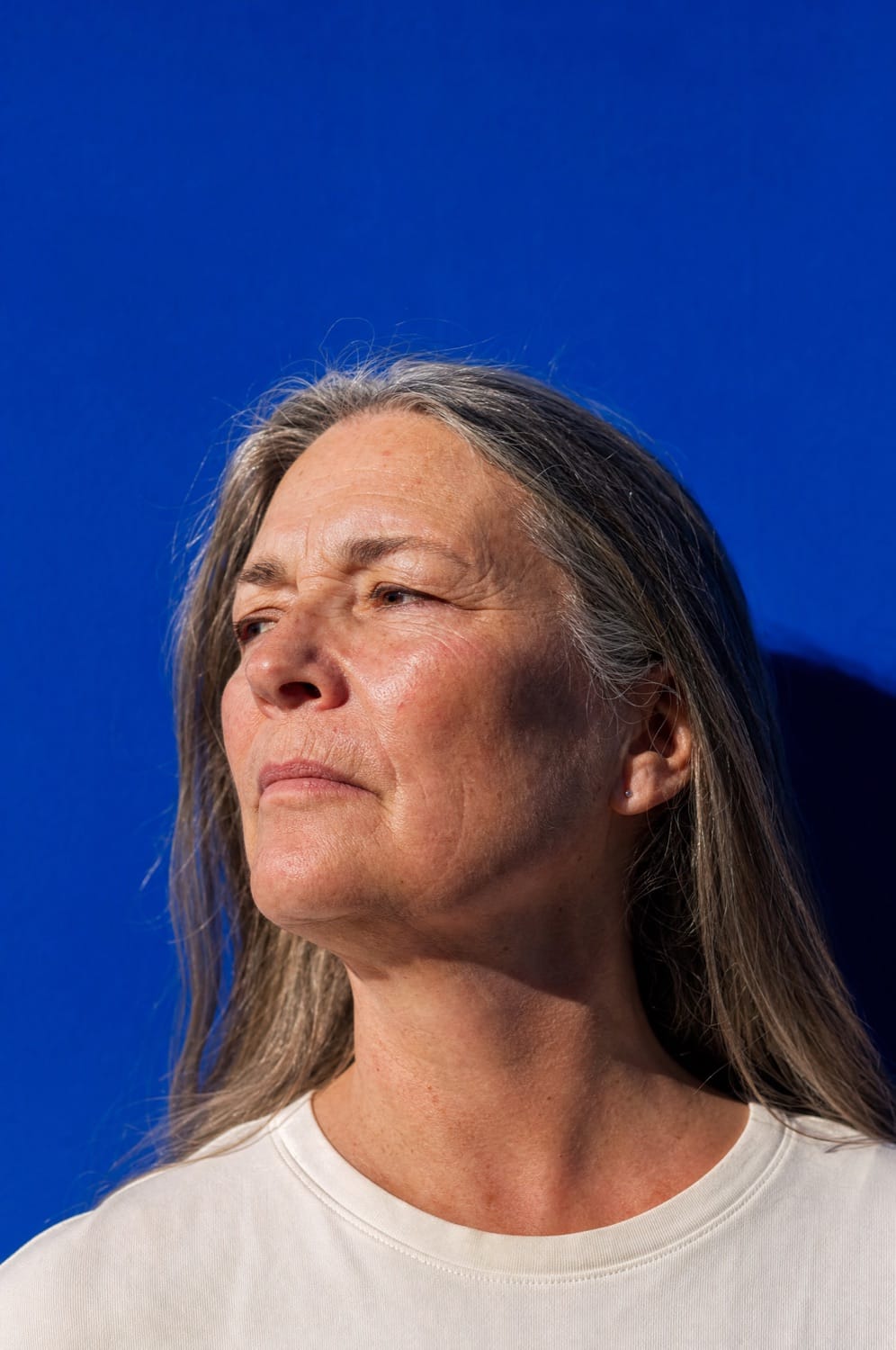 Frau um die sechzig im Profil vor kräftig blauer Wand, ruhig und entschlossen